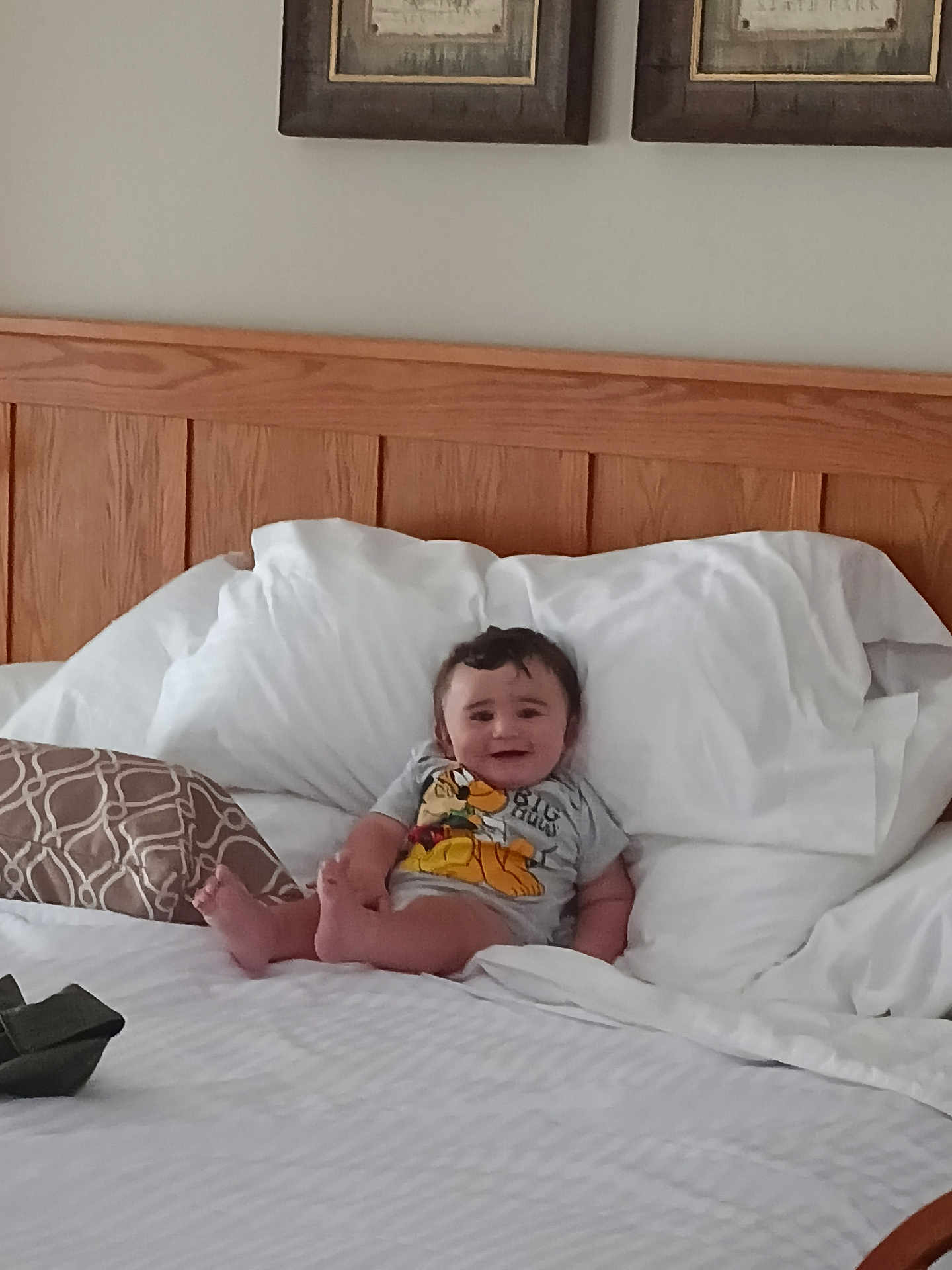 Maverick joined the competition — help win amazing prizes! baby, child, bed, pillow, smiling, indoors, wooden_headboard, white_bedspread, cartoon_shirt, feet, happy, person, portrait, relaxed, cushion, home_interior, wall_art, infant, sleeping_area, cozy