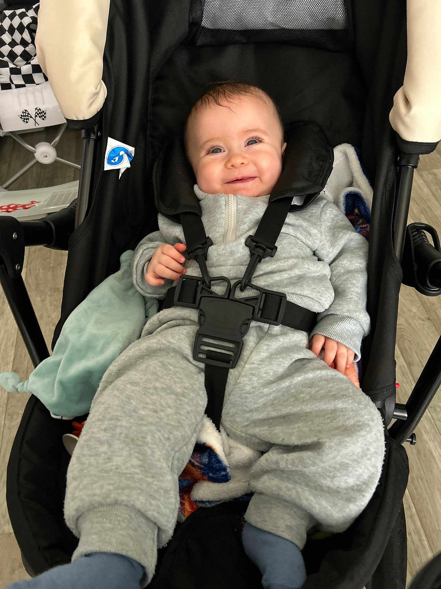 élio a rejoint le concours — aidez-le/la à gagner de superbes lots ! baby, infant, smiling, stroller, harness, buckle, blanket, onesie, gray_clothes, socks, wood_floor, seat, portrait, closeup, happy, hand, face, toy_pattern, cozy, indoor