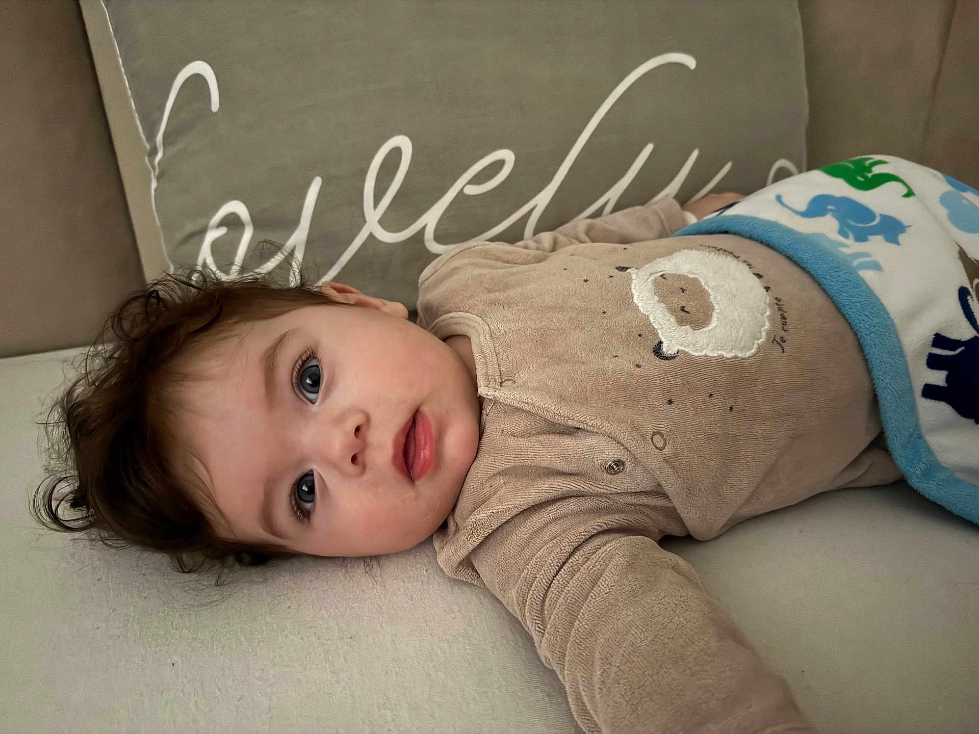 Aris participe au concours pour gagner de l'argent avec cette photo : baby, child, couch, blanket, pillow, onesie, sheep_design, face, blue_eyes, curly_hair, infant, indoor, laying_down, soft_lighting, cozy, cute, portrait, expression, sleepwear, homedecor