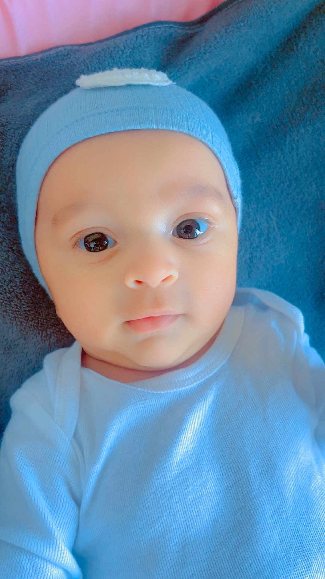 Maélio participe au concours pour gagner de l'argent avec cette photo : baby, infant, newborn, beanie, hat, onesie, close_up, portrait, big_eyes, blanket, towel, soft_texture, cute, adorable, face, skin, gaze, laying_down, pink_background, neutral_expression