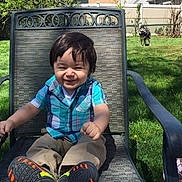 Christopher joined the competition — help win amazing prizes! toddler, child, smiling, outdoor, grass, chair, plaid_shirt, pants, shoes, dog, fence, backyard, sunny, happy, person, patio, greenery, casual_clothing, daytime, seated