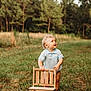 toddler, child, outdoor, grass, wooden_chair, curly_hair, blue_shirt, nature, field, trees, standing, baby, summer, greenery, cute, portrait, daylight, curious, small_furniture, happy