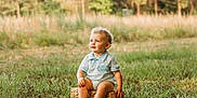 Wrangler is registered to the contest to win money with this photo: toddler, child, grass, outdoor, nature, basket, curly_hair, blue_eyes, sunlight, portrait, sitting, greenery, field, casual_clothing, shorts, summer, cute, baby, happy, innocent