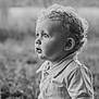 child, toddler, curly_hair, portrait, black_and_white, outdoor, grass, shirt, collar, side_profile, face, young_child, expression, cute, innocent, nature, soft_focus, baby, person, monochrome