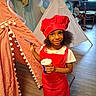 child, girl, chef_hat, red_outfit, paintbrush, cup, indoor, teepee, balloons, floor, couch, boy, window, curtains, wooden_floor, smile, playtime, party, decorations, shoes