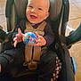 baby, car_seat, smiling, child, toy, indoor, happy, seatbelt, floor_tiles, clothing, infant, person, playful, cute, young_child, hands, face, seat, colorful, expression