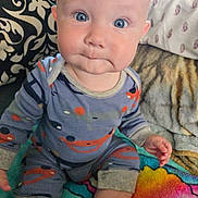 Hudson joined the competition — help win amazing prizes! baby, child, blue_eyes, onesie, sitting, blanket, pillow, patterned_clothing, indoors, cute, infant, face, hand, footwear, colorful, cozy, expression, soft_fabric, head, person