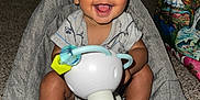 Julian is registered to the contest to win money with this photo: baby, smiling, toy, indoor, baby_seat, carpet, person, happy, child, foot, clothing, face, head, sitting, room, wall, door, bag, furniture, curly_hair
