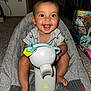 baby, smiling, toy, indoor, baby_seat, carpet, person, happy, child, foot, clothing, face, head, sitting, room, wall, door, bag, furniture, curly_hair