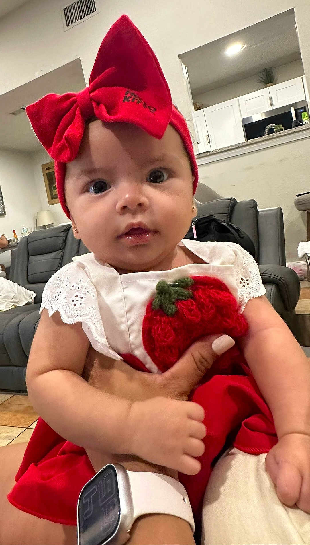 Aislin is registered to the contest to win money with this photo: baby, child, red_bow, headband, dress, indoor, living_room, person, cute, infant, hand, watch, couch, furniture, white_wall, curious, closeup, adorable, portrait, holding