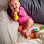 baby, bed, blanket, chewing, child, colorful, comfort, cute, foot, hand, happy, indoors, infant, person, pillow, pink_onesie, playing, relaxed, smiling, toy