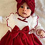 baby, infant, child, red_bow, headband, white_blanket, red_dress, long_sleeves, ruffles, cute, portrait, indoors, soft_texture, clothing, fashion, face, person, laying_down, closeup, adorable