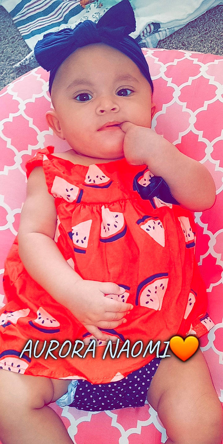 Aurora is registered to the contest to win money with this photo: baby, baby_toddler_clothing, cheek, child, dress, face, finger, hand, happy, headwear, lip, magenta, orange, person, pink, product, red, skin, sleeve, smile