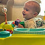 activity_center, baby, child, clothing, colorful, cute, face, furniture, hand, happy, head, indoor, infant, living_room, person, play, seat, smiling, toy, young_child