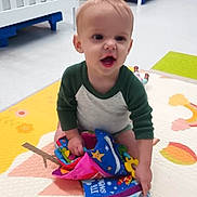 Kyl is registered to the contest to win money with this photo: baby, bright, child, clothing, colorful, crib, cute, early_childhood, floor, happy, indoor, person, playmat, playroom, sitting, smiling, soft_book, toddler, toy, young_child