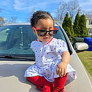 Jasmine is registered to the contest to win money with this photo: accessory, baby, blue_sky, car, child, confident, cute, fashion, grass, hood, outdoor, person, playful, red_tights, residential_area, sunglasses, sunny, toddler, trees, white_dress