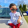 accessory, baby, blue_sky, car, child, confident, cute, fashion, grass, hood, outdoor, person, playful, red_tights, residential_area, sunglasses, sunny, toddler, trees, white_dress