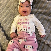 Kaylanna is registered to the contest to win money with this photo: baby, smiling, headband, hello_kitty, pink_pants, white_shirt, text_on_clothing, blanket, soft_texture, infant, happy, cute, child, lying_down, indoor, portrait, clothing, baby_girl, face, person