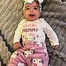 baby, smiling, headband, hello_kitty, pink_pants, white_shirt, text_on_clothing, blanket, soft_texture, infant, happy, cute, child, lying_down, indoor, portrait, clothing, baby_girl, face, person