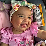 Kaylanna joined the competition — help win amazing prizes! accessory, apparel, baby, baby_girl, car_seat, child, closeup, clothing, cute, face, happy, headband, infant, person, pink_shirt, portrait, seat, smiling, text, young_child