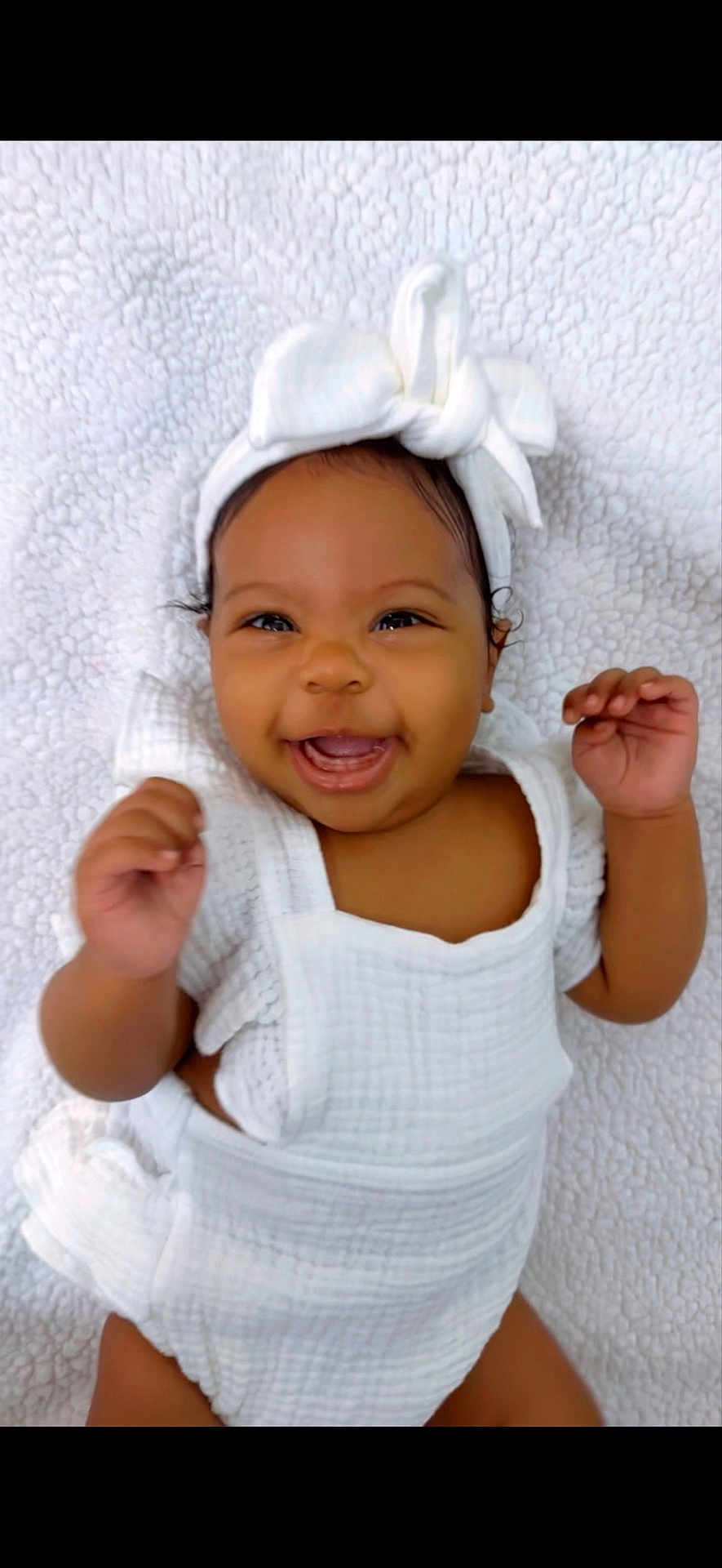 Camilla is registered to the contest to win money with this photo: baby, smiling, white_clothing, headband, bow, infant, happy, lying_down, blanket, soft_texture, cute, portrait, child, newborn, hands_up, indoors, closeup, face, skin, person
