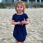 Macie is registered to the contest to win money with this photo: child, girl, beach, sand, dress, blue_dress, curly_hair, standing, outdoor, casual_clothing, sandy_ground, summer, young_child, person, portrait, natural_light, cute, small_child, vacation, innocent