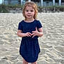 child, girl, beach, sand, dress, blue_dress, curly_hair, standing, outdoor, casual_clothing, sandy_ground, summer, young_child, person, portrait, natural_light, cute, small_child, vacation, innocent