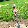 child, baseball_bat, grass, dirt, wooden_steps, cap, shorts, tshirt, outdoor, summer, greenery, playing, sport, boy, casual_clothing, shoes, recreation, nature, backyard, daytime