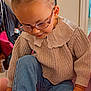 Larya participe au concours pour gagner de l'argent avec cette photo : child, glasses, hair_buns, sweater, lace_collar, jeans, socks, indoor, sitting, cute, smiling, young_child, portrait, cozy, casual_clothing, hand, footwear, home, furniture, playful
