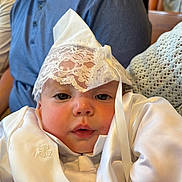 Bradley is registered to the contest to win money with this photo: adorable, adult, baby, ceremony, child, closeup, cuddled, eyes, face, family, formalwear, indoor, infant, lace_bonnet, photography, portrait, satin, seated, soft_lighting, white_outfit