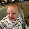 baby, bib, blond_hair, blue_eyes, cabinets, car_pattern, child, close_up, countertop, family_photo, happy, high_chair, home, indoor, infant, kitchen, open_mouth, portrait, seated, smiling
