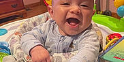 Clayton is registered to the contest to win money with this photo: baby, smiling, toy, piano, colorful, pajamas, indoor, wooden_furniture, book, playtime, child, happy, infant, face, hands, floor, door, dresser, plastic_toys, room