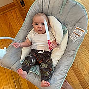 Clayton is registered to the contest to win money with this photo: baby, infant, baby_seat, wooden_floor, paper_knife, handmade_toy, white_shirt, animal_print_pants, cushion, foot, expression, indoor, child, person, clothing, comfortable, playful, curious, seat, home