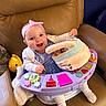Everleigh is registered to the contest to win money with this photo: baby, child, headband, blue_dress, activity_center, toy, basket, couch, leather, smiling, happy, indoor, sitting, white_socks, cute, playtime, infant, person, pink, colorful