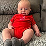 baby, infant, red_onesie, milk_carton_graphic, gray_socks, quilted_couch, leather_furniture, blanket, blue_eyes, pout, sitting, indoors, cute, child, portrait, soft_lighting, texture, cozy, hand, footwear