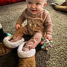 baby, child, infant, smiling, sitting, indoor, carpet, slippers, oversized_shoes, fuzzy, pink_outfit, toy, colorful_toy, dog, cushion, living_room, portrait, happy, playful, cozy