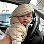 baby, child, hoodie, cap, steering_wheel, car_interior, wide_eyes, curious, person, infant, clothing, seat, hand, window, vehicle, portrait, cute, young_child, seatbelt, car_seat