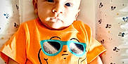 Enoan participe au concours pour gagner de l'argent avec cette photo : baby, infant, child, orange_tshirt, dinosaur_graphic, sunglasses, mickey_mouse_pattern, blanket, lying_down, cute, portrait, young_child, serious_expression, indoor, soft_lighting, hand, fist, head, face, toddler