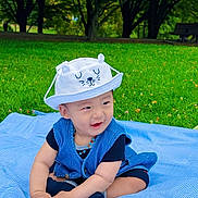 Tenzin Dawa participe au concours pour gagner de l'argent avec cette photo : baby, infant, toddler, child, hat, smile, blanket, grass, park, trees, outdoors, picnic, blue_clothing, necklace, sitting, portrait, cute, happy, playful, greenery