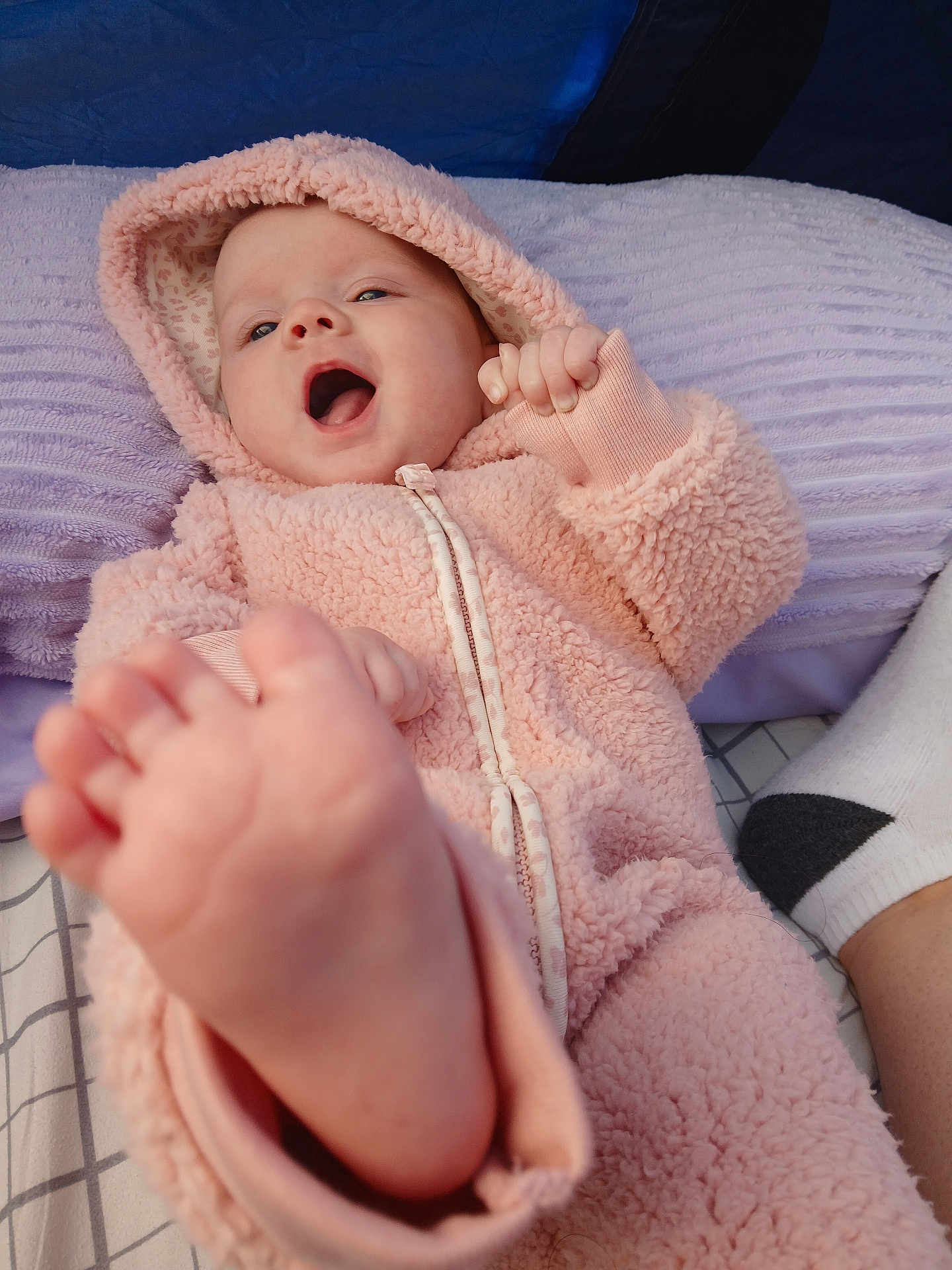 Elizabeth is registered to the contest to win money with this photo: baby, foot, pink_hoodie, happy, smile, pillow, blanket, sock, closeup, infant, face, hand, soft_texture, cozy, child, apparel, indoor, portrait, cute, lying_down
