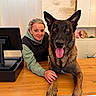 woman, dog, german_shepherd, pet, portrait, indoors, kitchen, counter, wooden_table, computer_monitor, sitting, tongue_out, happy, ears, black_and_brown, collar, human, animal, home, photography