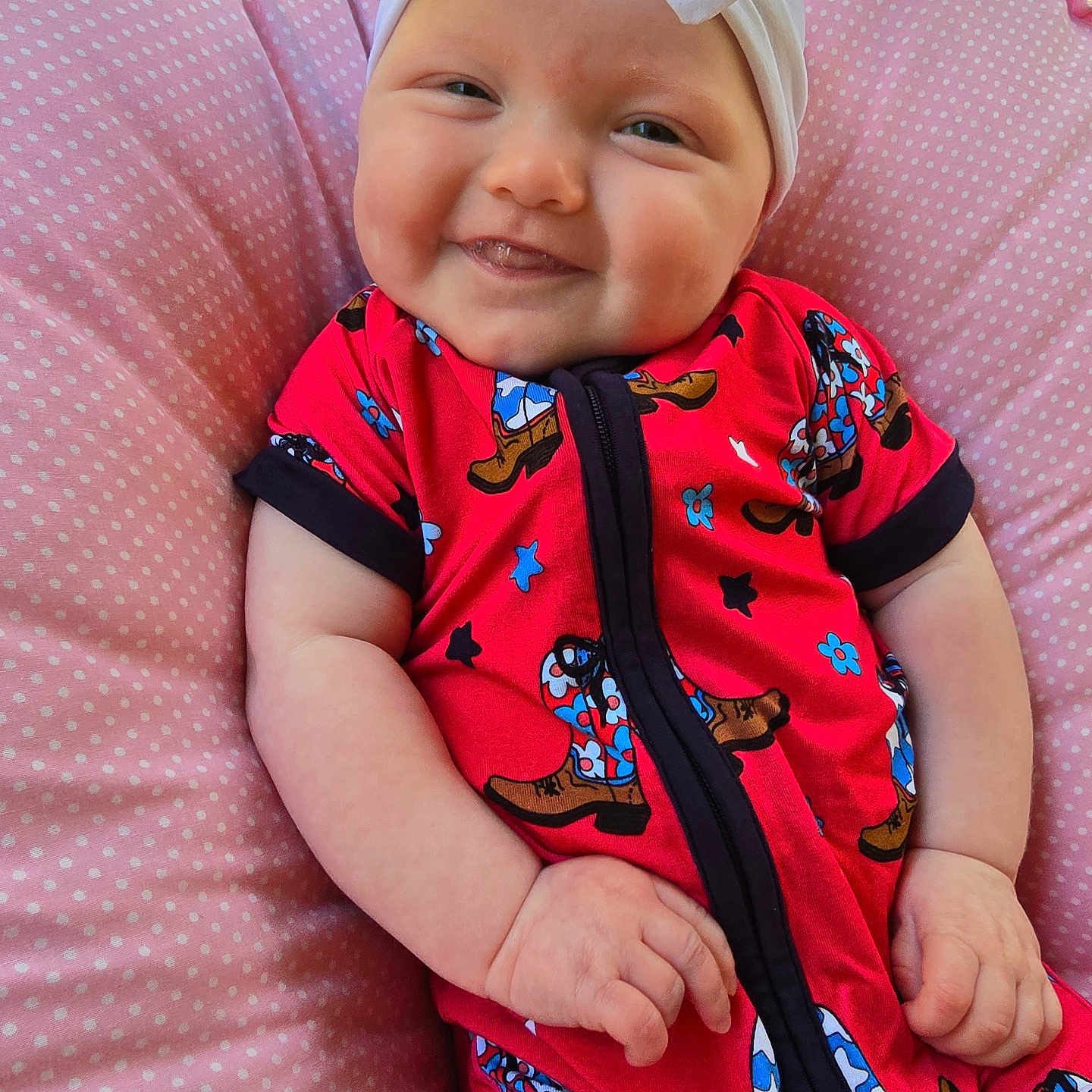 Remmie Kate is registered to the contest to win money with this photo: baby, child, closeup, cushion, cute, face, hands, happy, headband, indoor, infant, light, patterned_clothing, pink, polka_dot, portrait, red_clothing, relaxed, seated, smiling