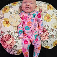 Remmie Kate joined the competition — help win amazing prizes! baby, infant, smiling, tongue_out, onesie, colorful_clothing, monster_pattern, floral_cushion, milestone_marker, 4_months, lying_down, happy, cute, child, indoor, portrait, face, person, baby_girl, playful