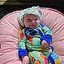 Remmie Kate joined the competition — help win amazing prizes! baby, child, infant, pajamas, hat, pink_cushion, indoor, smile, face, hand, colorful_clothing, patterned_outfit, cute, relaxed, seated, soft_furniture, playful, cozy, cheeky, portrait