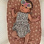 baby, infant, sunglasses, flower_pattern, cushion, crib, mesh, sleepwear, cute, child, portrait, resting, indoor, newborn, fashion, pink, white, floral, accessory, relaxing