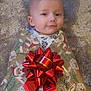 baby, child, face, smile, wrapping_paper, red_bow, christmas_theme, carpet, soft_texture, holiday, present, cute, infant, indoors, portrait, festive, wrapped, happy, cozy, gift