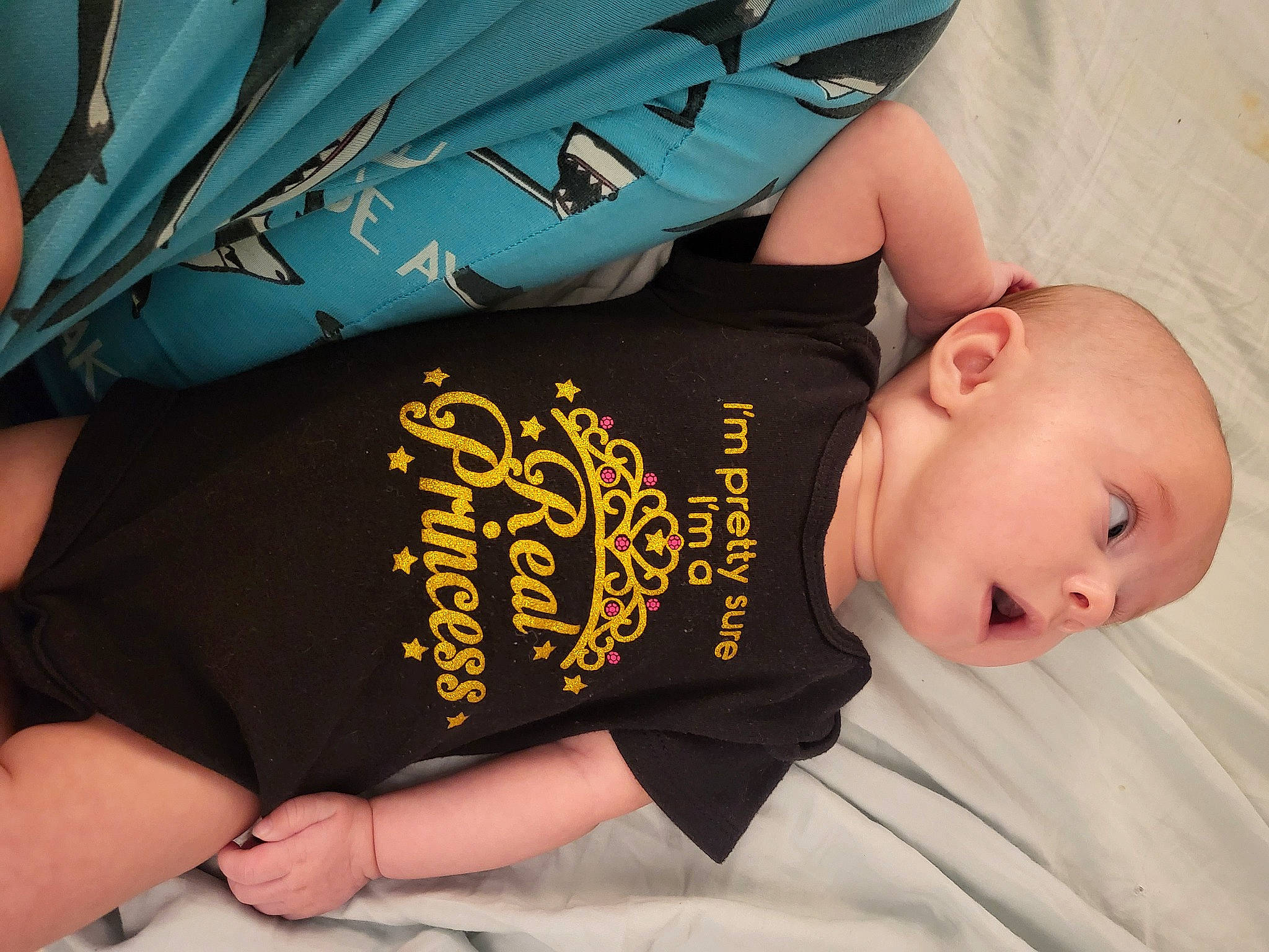 Lydia is registered to the contest to win money with this photo: arm, baby, baby_toddler_clothing, child, comfort, elbow, finger, font, gesture, human_body, joint, nail, neck, person, skin, sleeve, t_shirt, thigh, thumb, toddler