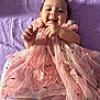 baby, infant, smile, tongue, pink_dress, floral_pattern, fabric, purple_background, cute, happy, lying_down, child, portrait, hands, feet, soft_lighting, face, tulle, delicate, young