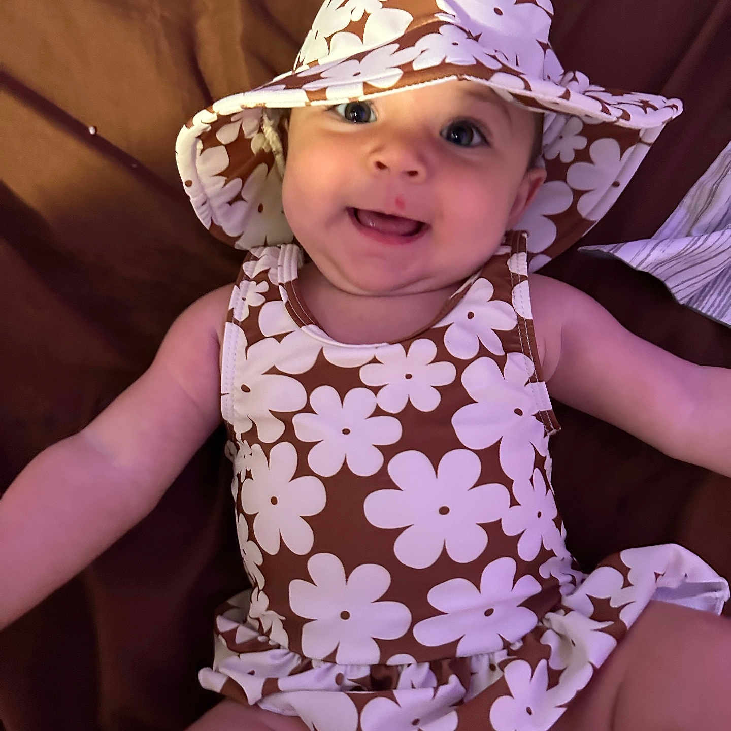 Alidia is registered to the contest to win money with this photo: apparel, baby, baby_girl, brown, child, clothing, cute, face, floral_pattern, happy, hat, headwear, indoors, infant, person, portrait, sitting, skin, smiling, white