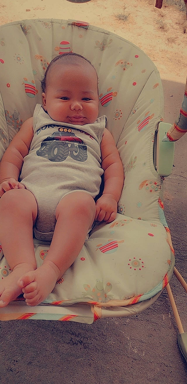 Joseph is registered to the contest to win money with this photo: baby, baby_products, baby_toddler_clothing, cheek, child, comfort, eye, facial_expression, hairstyle, happy, human_leg, pattern, person, pink, sitting, skin, sleeve, smile, stomach, thigh